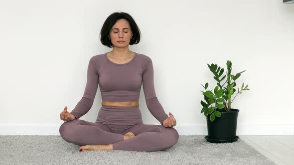 Pretty fitness young woman in violet sportswear practicing yoga exercise in lotus pose