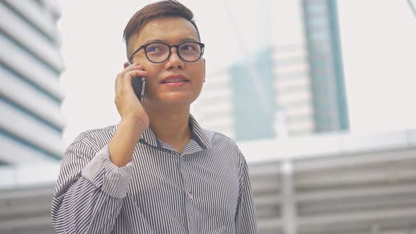 Asian men with glasses use phones in street near big office buildings.