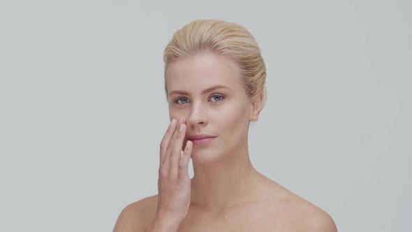 Studio portrait of young, beautiful and natural blond woman applying skin care cream. F alt