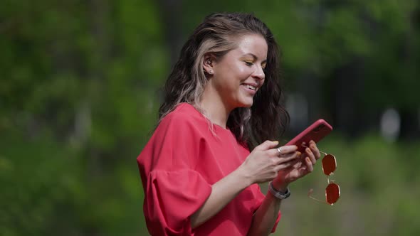 Woman is Sending Voice Message By Mobile Phone Walking in Park Positive Emotion and Good Mood alt
