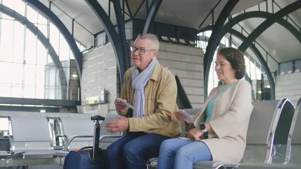 Aged Couple Sitting at Railway Station and Checking Train Tickets Waiting for Boarding alt