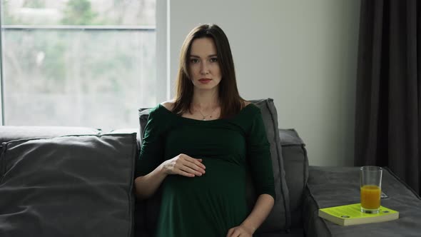 Portrait of Beautiful Pregnant Woman Sitting on Sofa and Gently Touching Her Belly alt