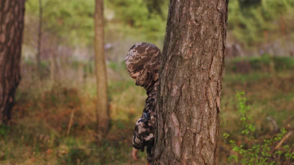 The Boy in Camouflage and Balaclava Jumps Out of the Ambush with Wooden Gun