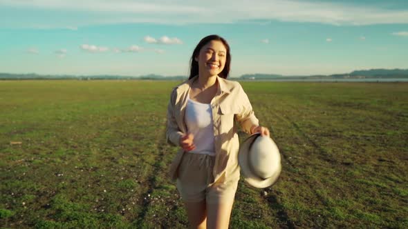 slow-motion of cheerful woman walking across the green field with sunlight
