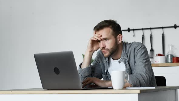 A Young, Thoughtful Freelance Man Looks at the Monitor Screen, Works at a Computer in A Room at Home