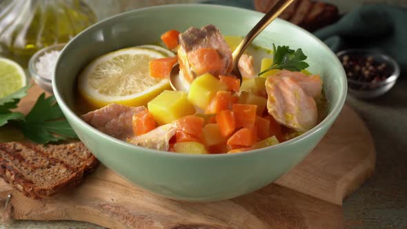 Stiring a Salmon Creamy Soup with Carrots and Potato in a Green Plate alt