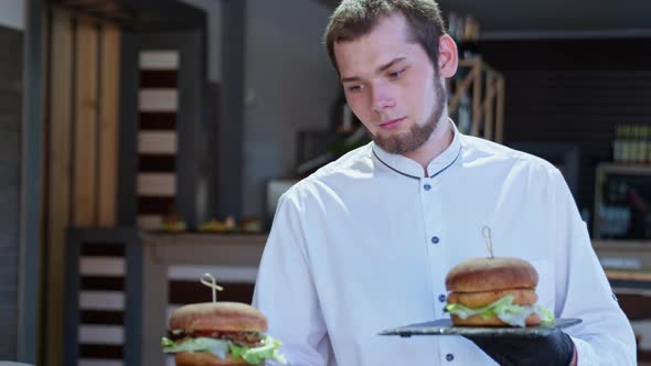 Nice Waiter Makes Tasty Juicy Burgers To Joyful and Hungry Visitors of Happy Family with Children alt