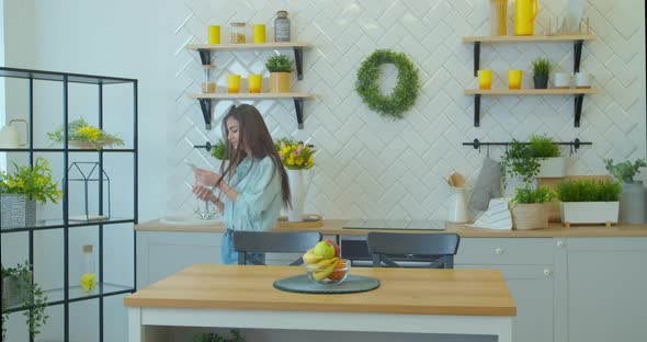 Young Attractive Woman in Positive Mood Is Dancing in Kitchen, Wearing Wireless Headset, Listening alt