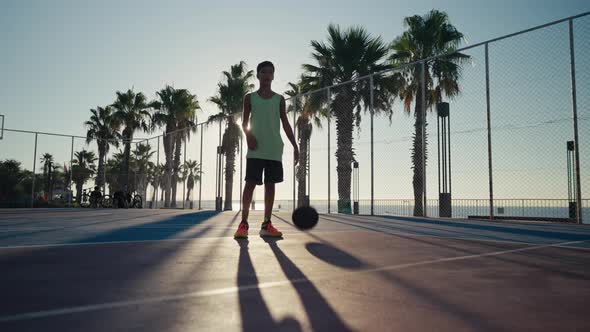 12 Year Old Boy Bouncing Basketball Ball Training on Ground Floor of the Court alt