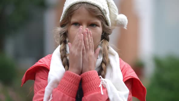 Portrait of Charming Teenage Caucasian Girl Blowing on Palms Rubbing Hands Standing Outdoors on alt