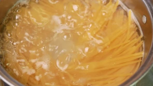 Raw spaghetti is being cooked in boiling water in a kitchen pot. alt