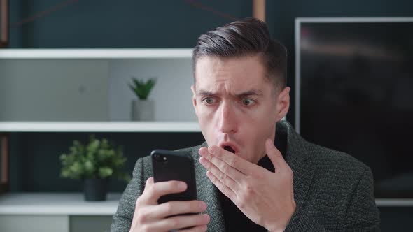 Stressed Businessman is Shocked While Using Smartphone on Modern Office Background
