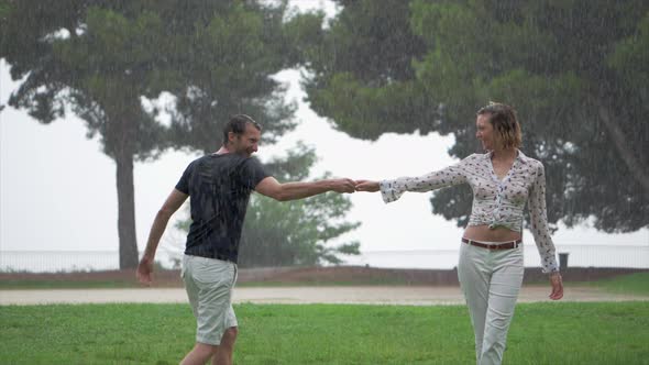 A Romantic Couple Joyfully Dancing Around Each Other in the Pouring Rain at a Park, Slow Motion, Sta alt