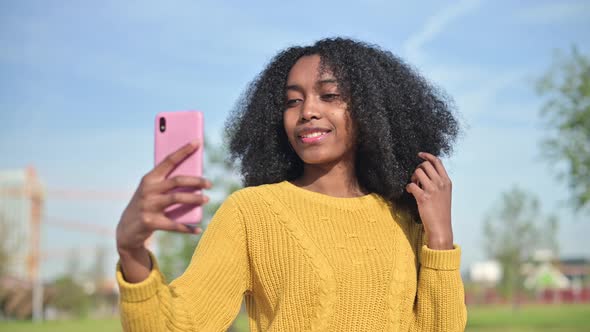 young black african woman in a yellow sweater makes a selfie on the phone alt