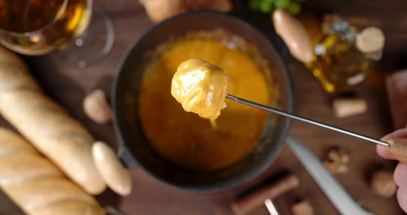 Male Hand Dips a Piece of Bread in Fondue. On Wooden Background alt