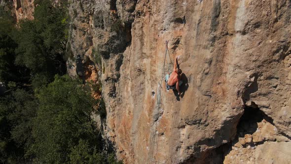 Aerial View From Drone of Strong Muscular Young Man Climbs on Big Rocky Wall By Challenging Rock alt