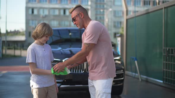 Proud Caucasian Father Talking with Son Standing at Clean Vehicle at Car Wash Service Rubbing Child alt