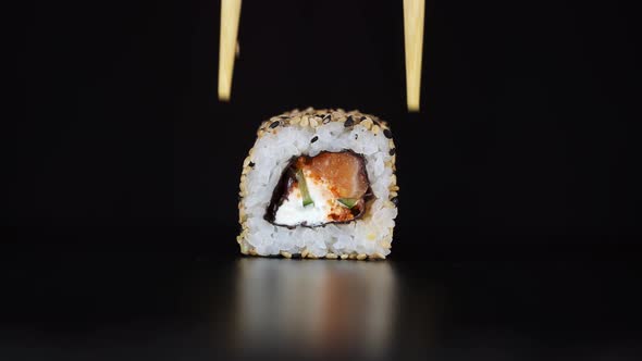 The Sushi Roll Is Lifted Up with Chopsticks. Japanese Food Black Background.