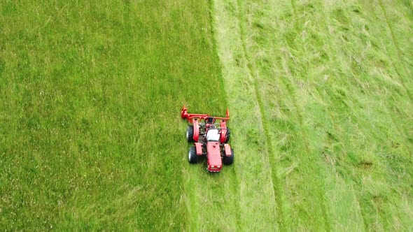 Red lawnmower tractor moving straight parallel rows of green grass. Aerial 4k view. alt