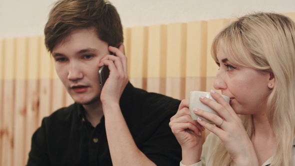 Couple sitting in cafeteria man calling by mobile phone