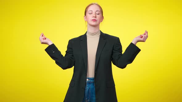 Portrait of Confident Slim Businesswoman in Suit Meditating in Lotus Pose at Yellow Background alt