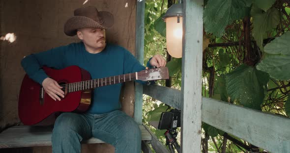 Man with an Guitar is Sitting on Porch Tuning Instrument Using an App on Phone alt