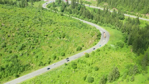 Aerial View of Serpentine Road with Driving Cars in Mountains with High Green Trees alt