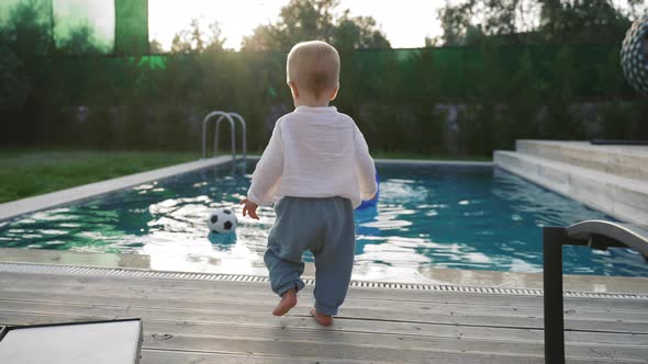 Toddler Walks to Take Soccer Ball Floating in Swimming Pool alt