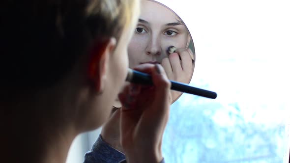 Woman Looking in the Mirror and Apply Makeup to the Face.