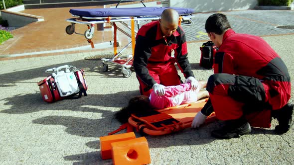 Paramedics putting injured girl onto a backboard alt