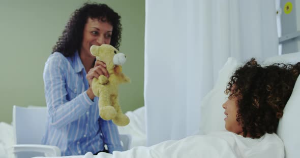 Front view of African american mother giving teddy bear to her son in the ward at hospital 4k alt