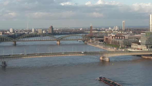 AERIAL: View Over Rhine River in Cologne Cargo Boat Going Under a Bridge in Beautiful Sunlight  alt