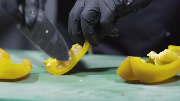 Cook's Hands in Black Gloves Chopping Yellow Peppers Close Up alt