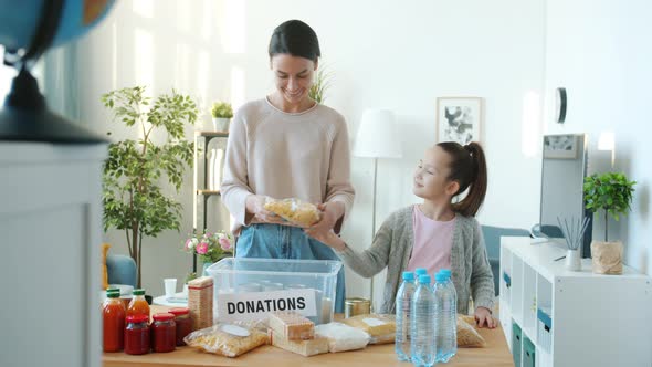 Mother and Daughter Packing Groceries for Donation While Father Bringing Boxes with Food at Home alt