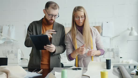 Male and Female Clothes Designers Working at New Garment and Using Tablet Indoors in Studio alt