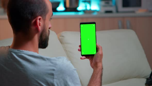 Relaxed Man Looking at Smartphone with Mock Up Green Screen Chroma Key Display alt