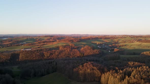Aerial footage of small villages and colourful trees at sunset in west Germany. Pull back shot revea alt