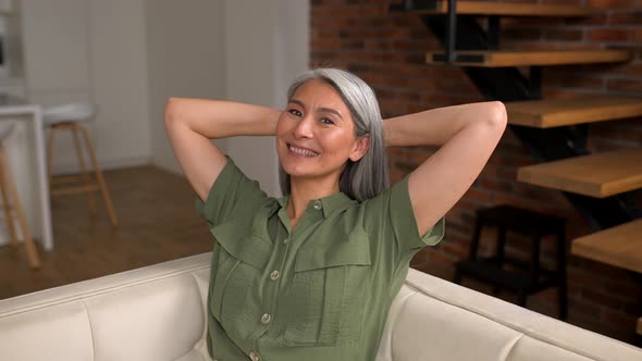 Serene Carefree Middleaged Woman with Long Gray Hair Sitting on Sofa in Modern Apartment