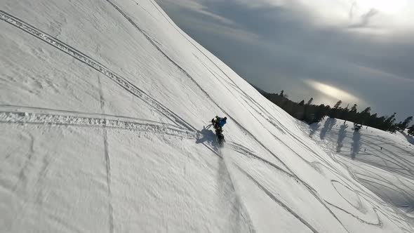 Aerial View Male Extreme Sports Snow Bike Riding From Mountain Summit with Snowy Splashes Tracks alt