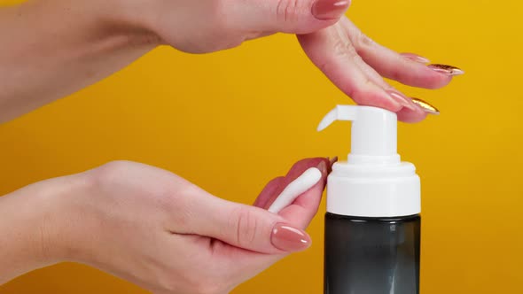 Female Hands Pushing Dispenser and Using Liquid Soap on Yellow Background alt