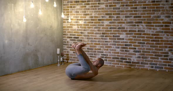A Muscular, Lithe, Bearded Man Does Yoga in a Gym Against a Brick Wall, He Sits on a Transverse alt
