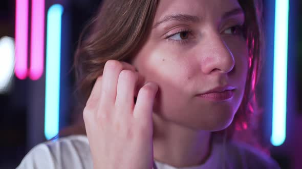 A Beautiful Woman Inserts Wired Headphones Into Her Ears in a Neon Room