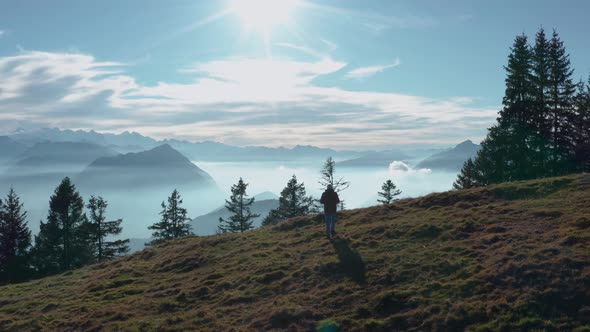 guy walking on a mountain ridge looking into beautiful mountain scenery with fog covered lake sunny alt