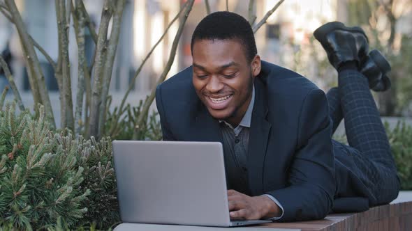 Smiling Confident Satisfied Young Adult Businessman or Corporate Employee Lying Down Uses Laptop alt