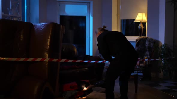 Wide Shot Caucasian Policeman Examining Crime Scene with Flashlight Indoors alt