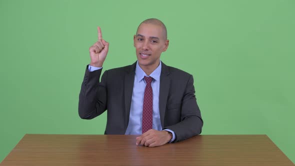 Happy Bald Multi Ethnic Businessman Pointing Up Behind Desk alt