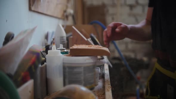 A Man Worker Shakes the Board From the Wooden Shavings and Takes It From the Stand alt