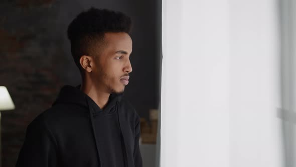 Thoughtful Black Man in Dark Hoodie Looks Out of Window alt