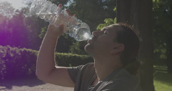 Handsome Man Drinking Water From a Plastic Bottle in the Park in the Sunshine
