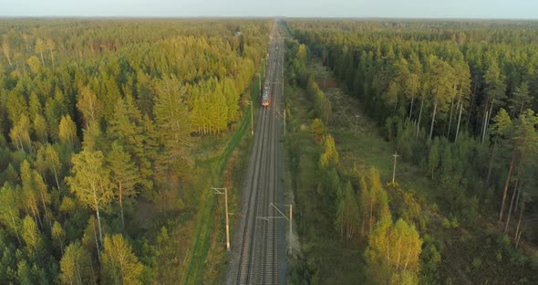 Aerial View of Fast Passenger Train Driving on Railroad in Forest at Sunset alt